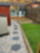 A garden pathway with black stone slabs surrounded by gravel, leading to a patio and a wooden shed in a landscaped yard