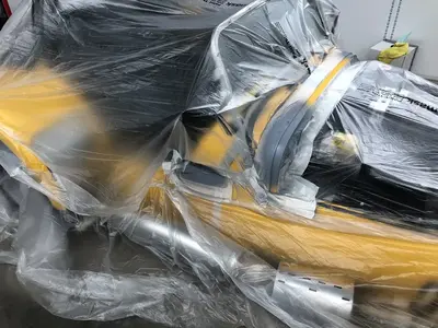 A yellow car covered in a thin transparent plastic sheet, partially revealing its sleek build