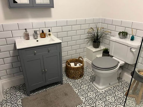A classic bathroom layout featuring a grey vanity unit, patterned flooring, and white brick tiles