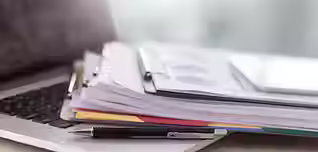 Close-up of a laptop keyboard with a stack of documents on top