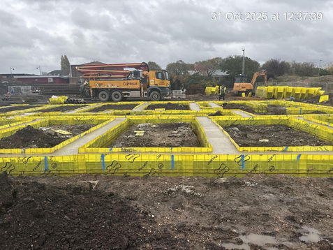 Construction site with yellow foundation molds forming a grid pattern on muddy ground