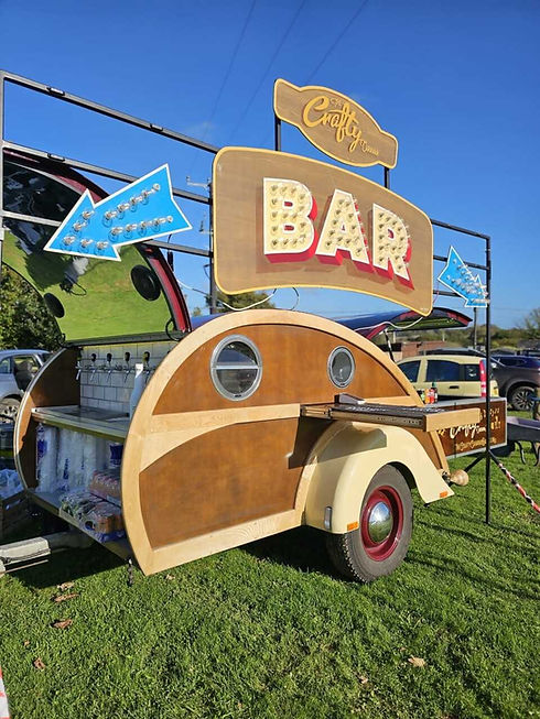 Retro-style mobile bar with large "BAR" sign and wooden accents, offering beer, cider, and prosecco