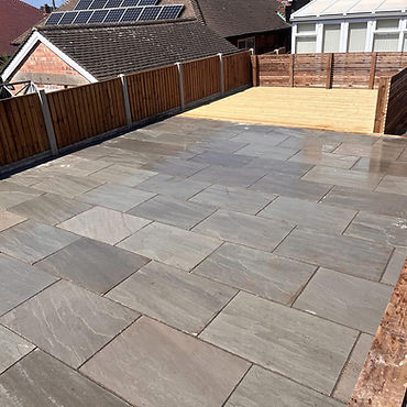 Newly paved patio with a wooden deck and fence under a sunny sky