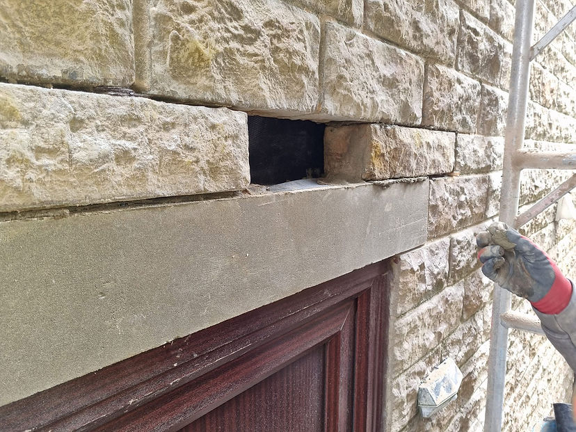 A close-up of a stone wall with a missing brick above a door