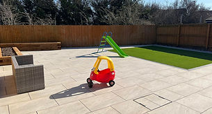 Paved garden patio featuring a child's toy lawnmower in the background