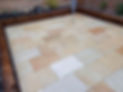 A patterned patio with various shades of beige and brown tiles, bordered by wooden beams
