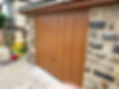 A wooden garage door with paneling is set against a stone wall