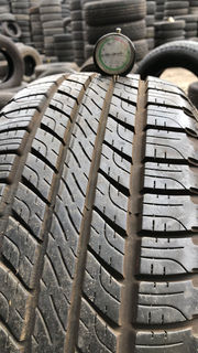 A tire with a gauge rests in front of a large stack of tires
