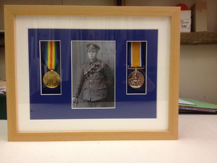 A soldier in uniform with medals, standing tall and proud in a framed photo.