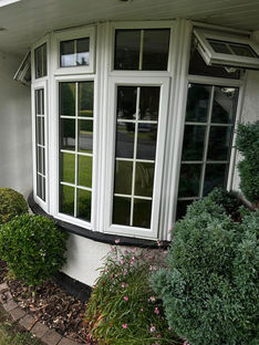 White bay windows with grid patterns on a house, surrounded by lush green bushes