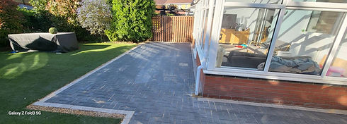 A newly laid grey block paved patio space running alongside a residential conservatory