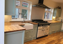 Bright kitchen with pastel green cabinets, wood countertops, a farmhouse sink, and a large vintage-style stove
