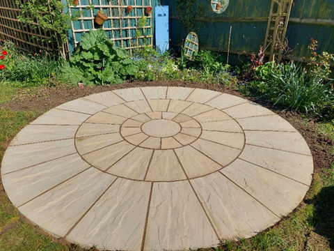 A circular patio featuring a smooth, circular stone floor surrounded by greenery