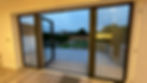 View from inside a home showing large glass doors opening to a wooden deck and garden