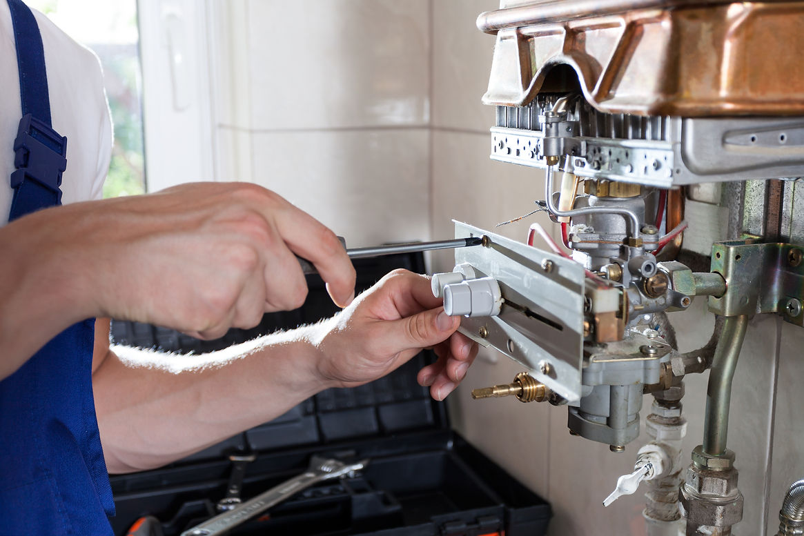 An engineer fixing a gas water heater with a screwdriver