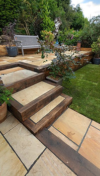Terraced garden with wooden steps and stone slabs leads to a wooden bench
