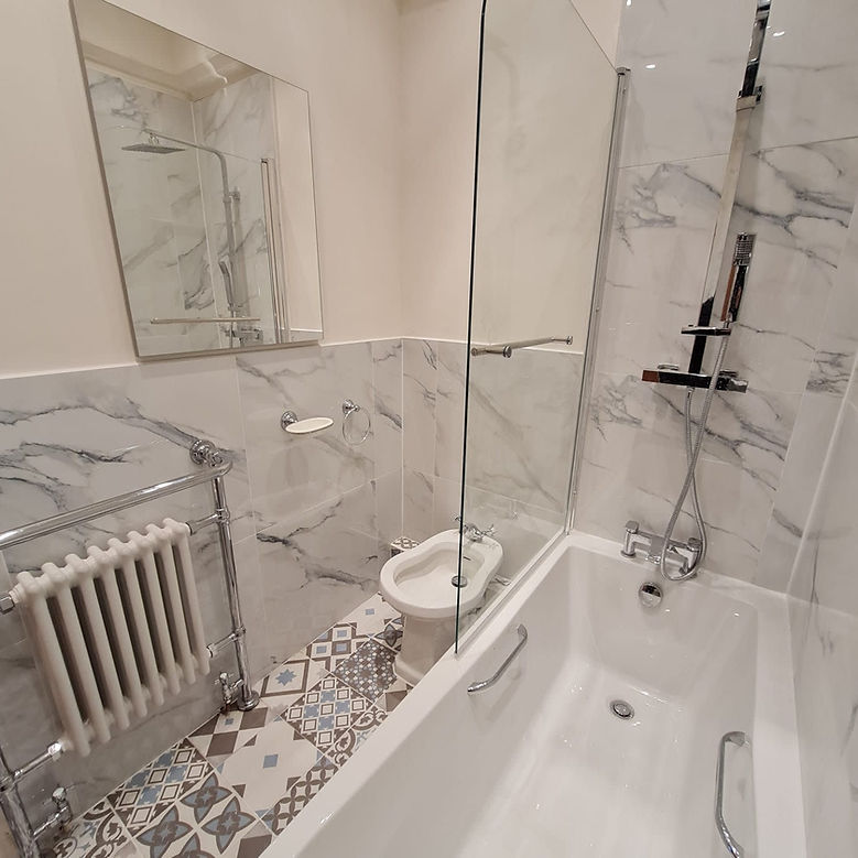 A bright luxury bathroom featuring a white bathtub, glass shower panel, and marble wall tiling