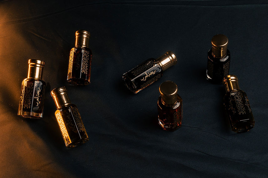 Six ornate perfume bottles with gold caps are arranged on a dark fabric surface