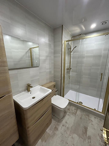 Modern bathroom with light gray tiles, featuring a glass shower enclosure with gold trim