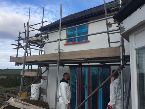 Workers in white protective gear assembling scaffolding alongside a residential renovation project