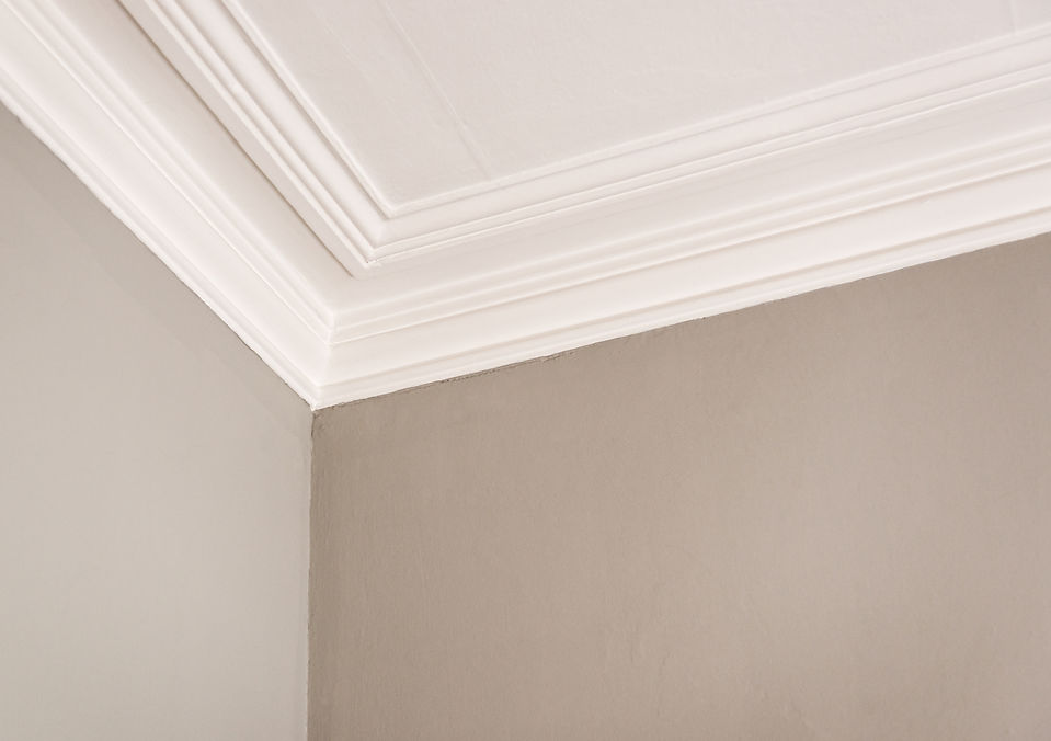 A beige corner ceiling with white decorative crown molding, creating a clean, elegant look