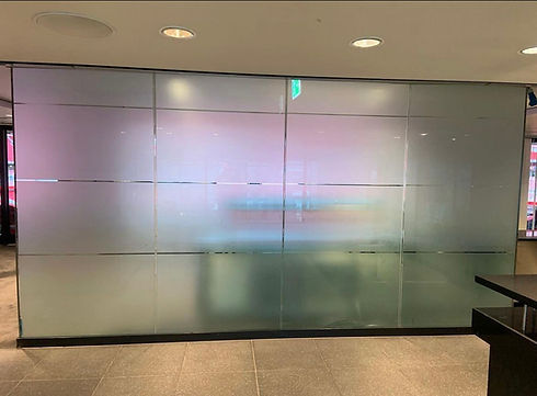 A large frosted glass wall in an office lobby displays a subtle gradient of pink to blue tones