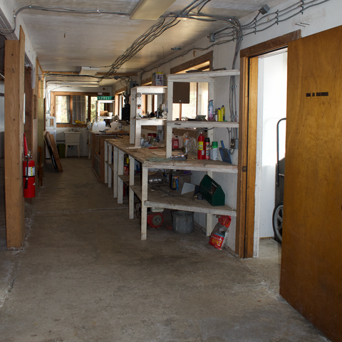 1st floor, daylight basement, looking north - work space / benches with solar battery bank in the middle, front entry on the left. Waterfront Homestead for sale, Kupreanof Island Alaska