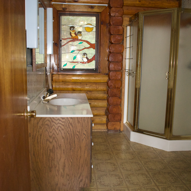 2nd floor, log interior, bathroom west facing window showing shower stall and sink, includes a toilet not seen in the image to the right.