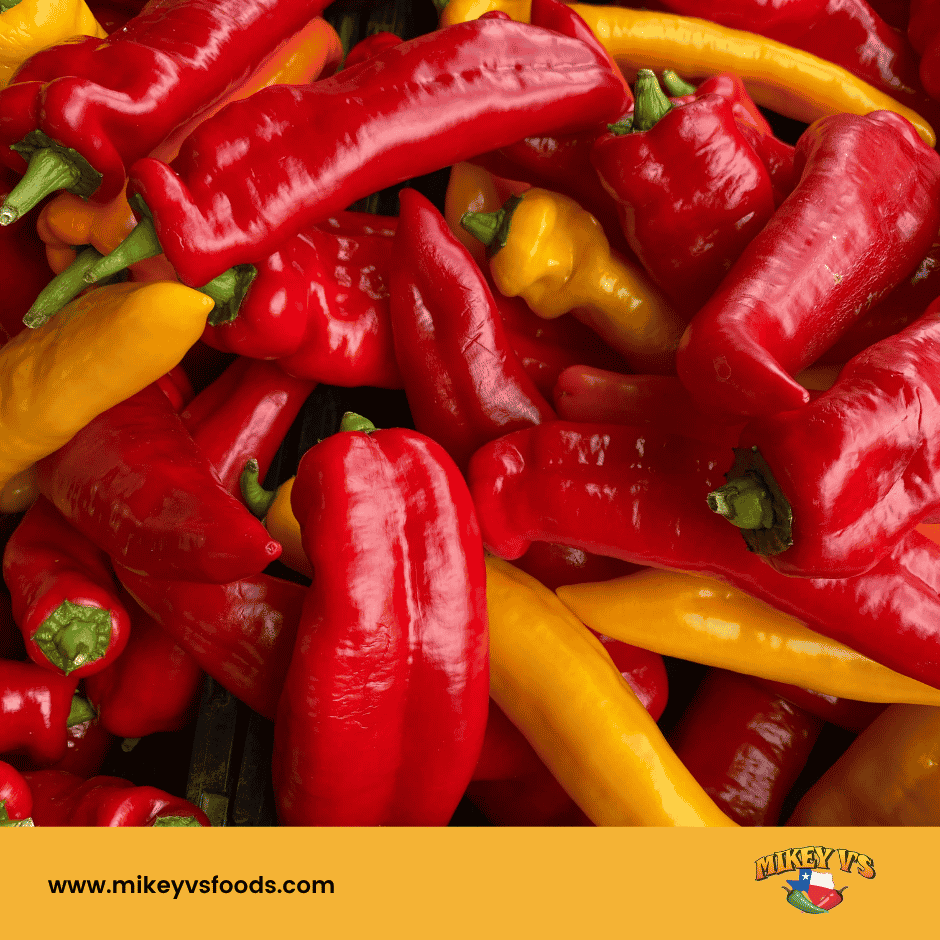 Red and yellow peppers stacked closely. Bright colors dominate. mikeyvsfoods.com text and logo at the bottom on a yellow background.