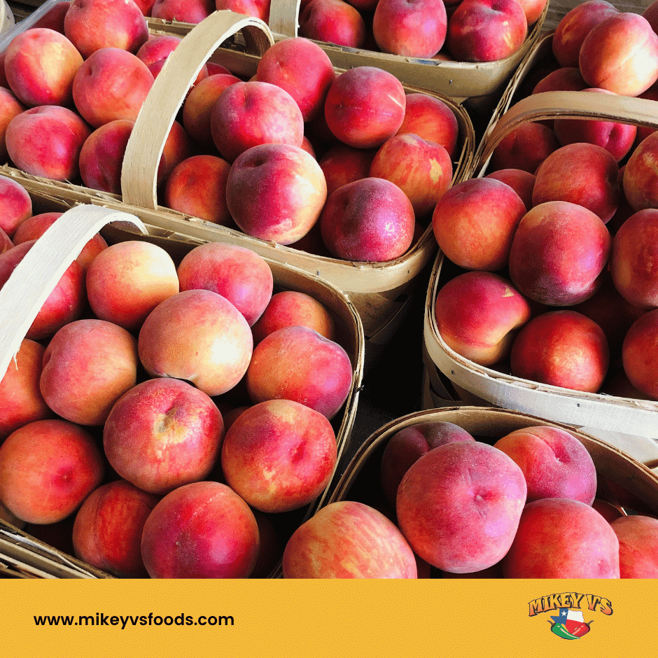 Baskets of ripe peaches at a market, with Mikey V’s logo and website www.mikeyvsfoods.com on a yellow banner.