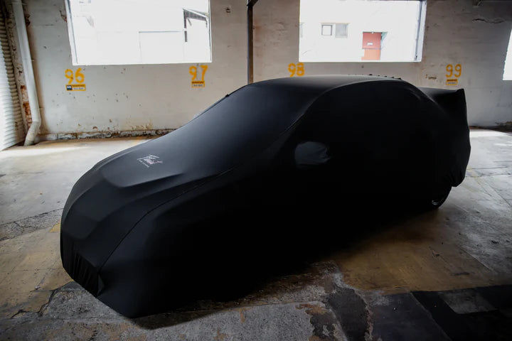Black car covered with a black car cover, 96, 97, 98, 99 visible on the wall
