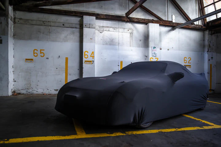 Black car covered in a garage with numbers 65, 64, and 62 on the walls