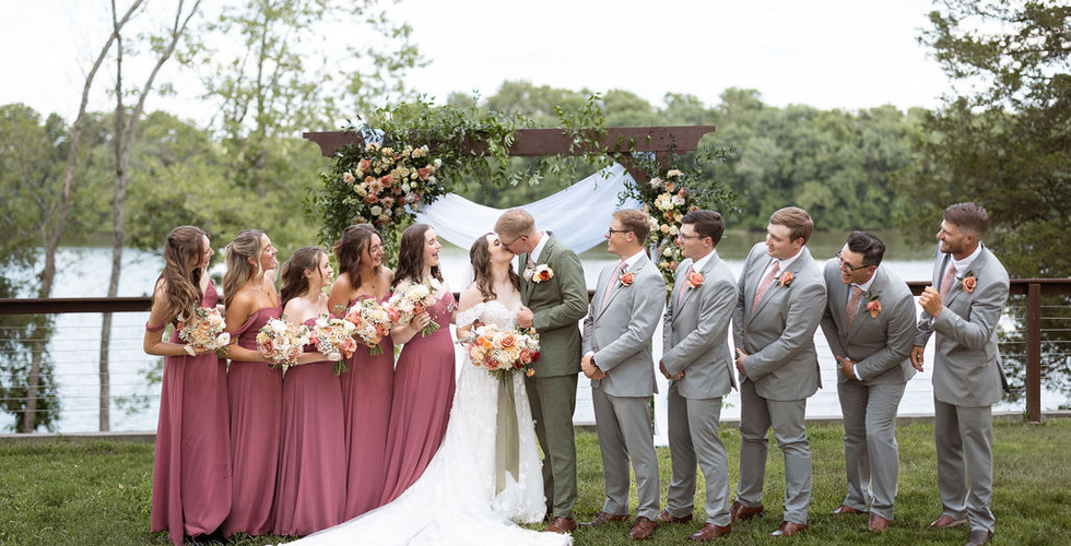 bride and groom kiss in front of wedding party