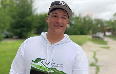 Dre Erwin posing for a picture in Regina Saskatchewan wearing a New York Yankees hat and a Dre Erwin Photography Sweater in white