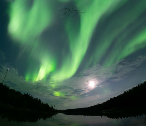 Bright green aurora borealis swirling over the dark landscape of Sandy Bay, Saskatchewan.