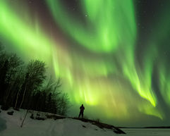 a photo of a man taking pictures of the aurora borealis in a winter scene