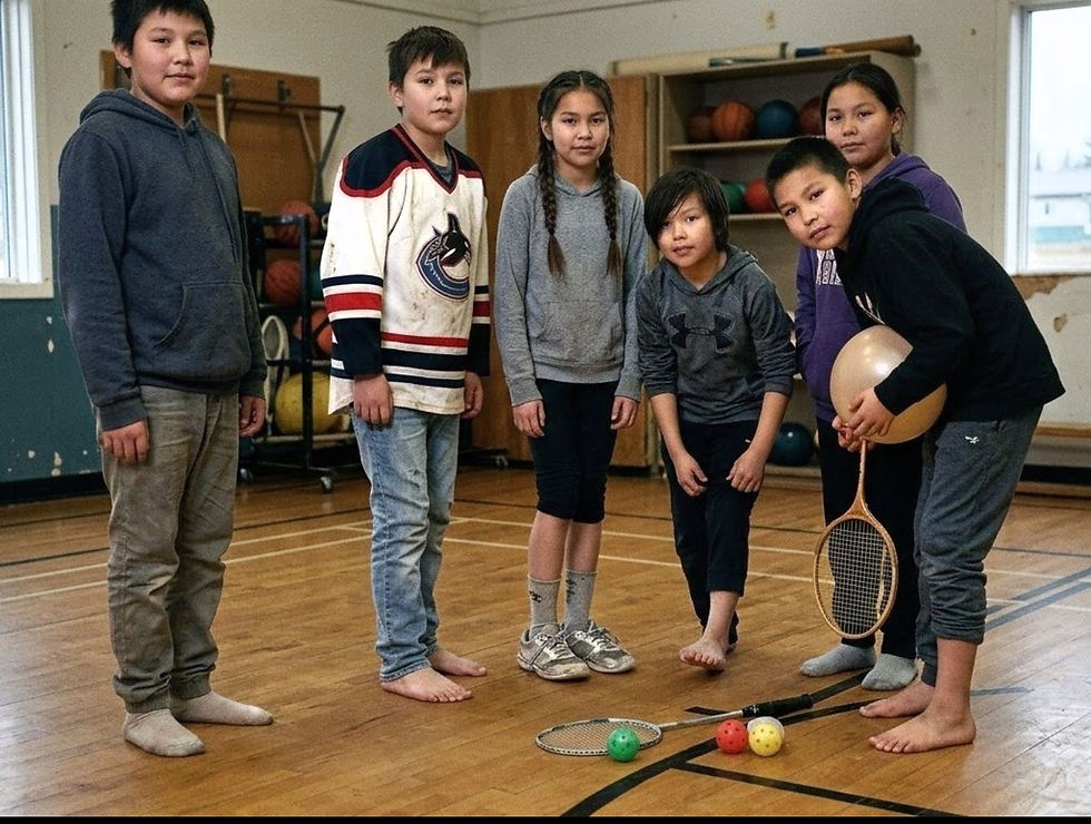 A group of six Indigenous youth stand on a wooden gym floor in Sandy Bay, Saskatchewan. One boy holds a beige balloon and a badminton racket, while others stand nearby—some in sneakers, one in socks, and another barefoot. The image captures the resilience of the community despite a stark lack of basic sports equipment and proper gym shoes.