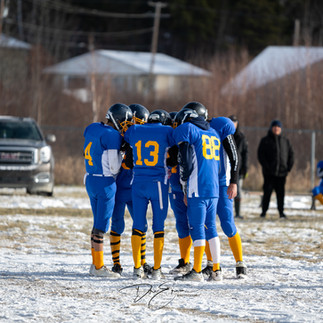 A group of youth athletes in blue and yellow jerseys huddled together on a snowy field. This captures the spirit of teamwork and the urgent need for sports equipment to support youth mental health.