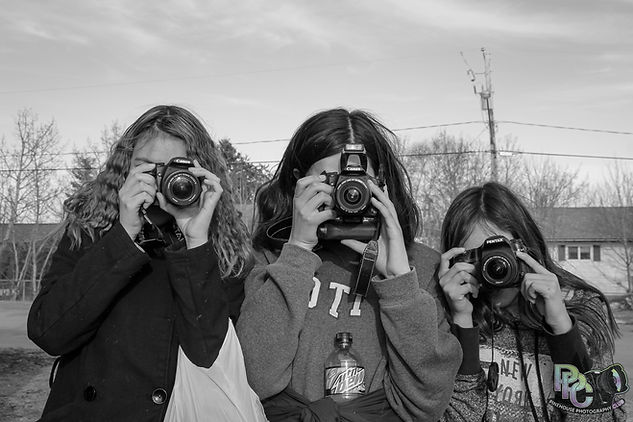 Three enthusiastic youth from the Pinehouse Photography Club engaging with cameras at Pinehouse Lake, symbolizing empowerment, creativity, and the positive impact of photography on youth mental health
