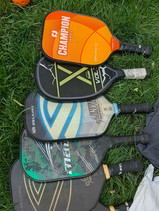 A crisp close-up photograph by Dre Erwin of four donated pickleball paddles resting on the lawn, representing the foundation of the new youth pickleball league designed to boost mental wellness and community connection.