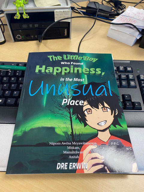 A paperback copy of the children's book The Little Boy Who Found Happiness in the Most Unusual Place by Dre Erwin on a desk.