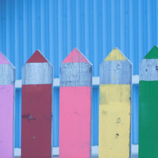 Close-up of a multicolored wooden picket fence against a blue wall. Emotional expression via Dre Erwin Photography.