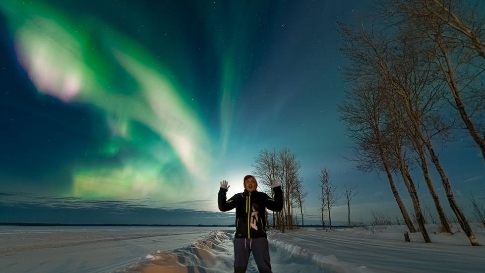 Man in front of the northern lights, in Pinehouse Lake