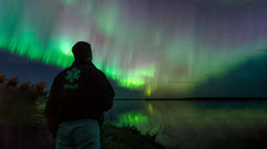 A peaceful moment of reflection as a person watches the green northern lights dance over a calm Saskatchewan lake by Dre Erwin.