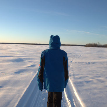 A person in a blue jacket walking away across a vast snow-covered field. Part of the Dre Erwin Therapeutic Photography initiative.