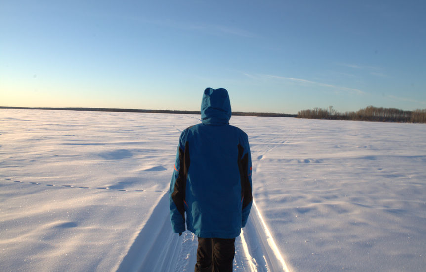 A person in a blue jacket walking away across a vast snow-covered field. Part of the Dre Erwin Therapeutic Photography initiative.