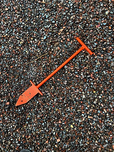 An orange tree planting bar laying flat on gravel