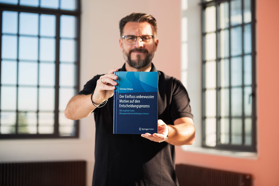 Mann in schwarzem Hemd hält ein Buch über unbewusste Motive und Entscheidungsprozesse – Symbol für Wissen und Erfolg.