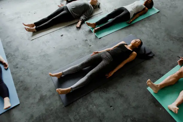 Participants lie in peaceful stillness during a yoga session, practicing the Corpse Pose on their mats.