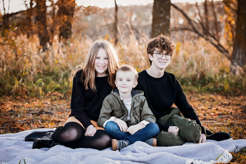 three young siblings sit on a blanket and smile during fall family photos in Blair, ne